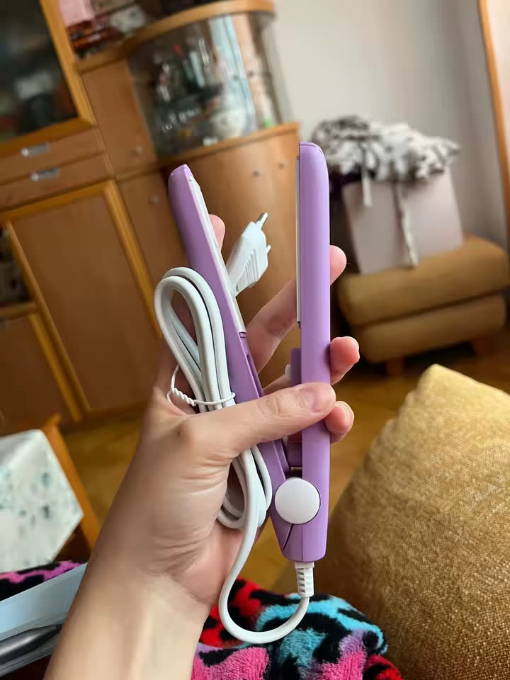 Mini lisseur violet tenu en main avec son cordon blanc